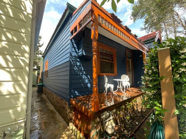 Navy blue weatherboard cottage with stained timber verandah at Camp Cove